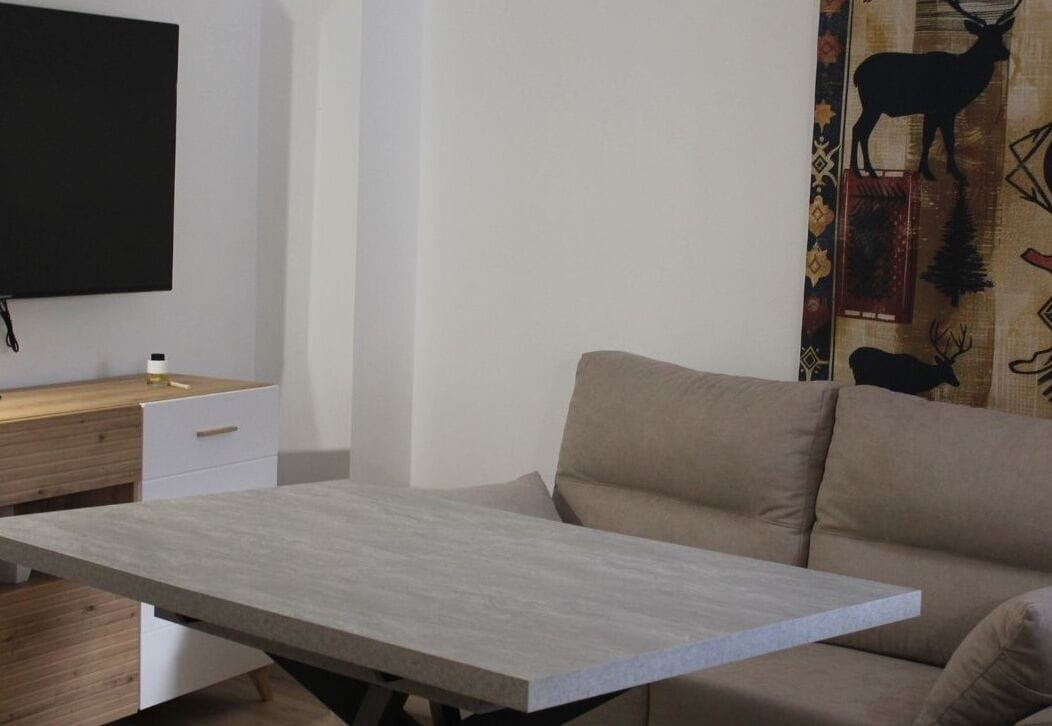 Una sala de estar moderna con un sofá, una mesa de centro, un televisor montado en la pared y un tapiz decorativo.