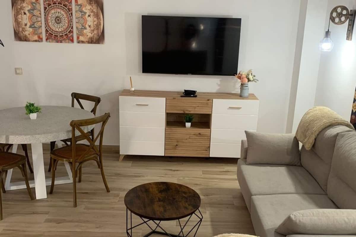 Ein Wohnzimmer mit Fernseher, einem Esstisch mit Stühlen, einer Couch und einem Couchtisch.