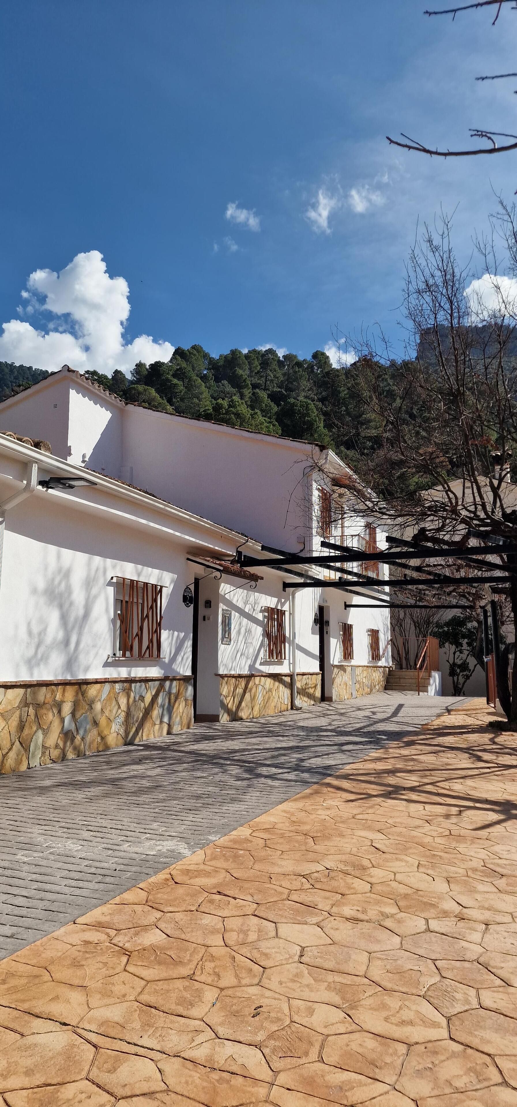 A white building with a stone base, a tiled patio, and a mountainous backdrop.