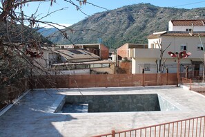 Situated in a hilly landscape, this building features a tiled roof and flat facade surrounded by a metal fence.