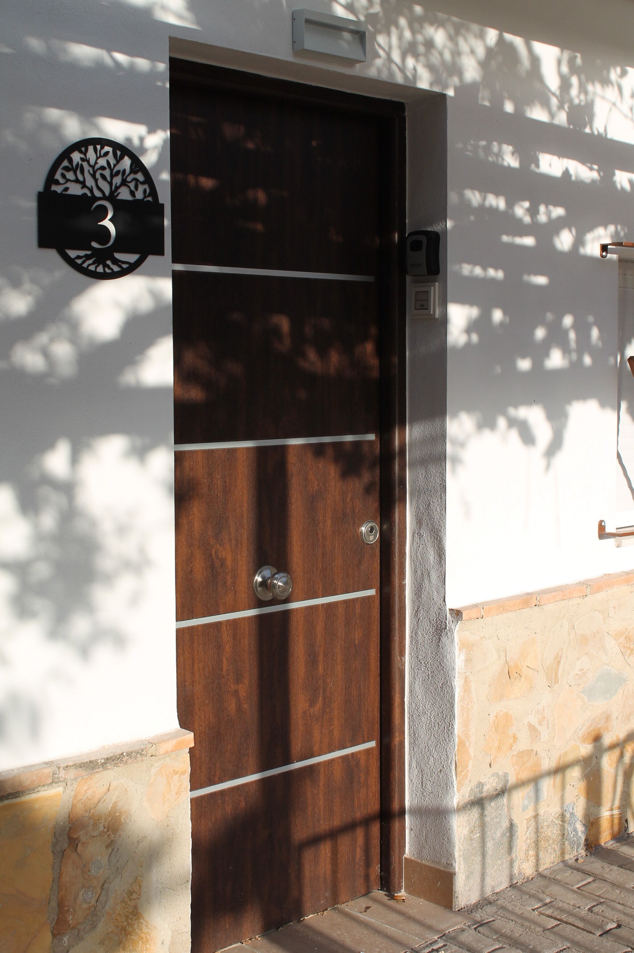 A wooden door with a number plate, a mailbox, and a wall-mounted light fixture.