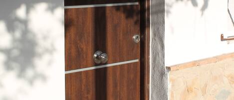 A wooden door with a number plate, a mailbox, and a wall-mounted light fixture.
