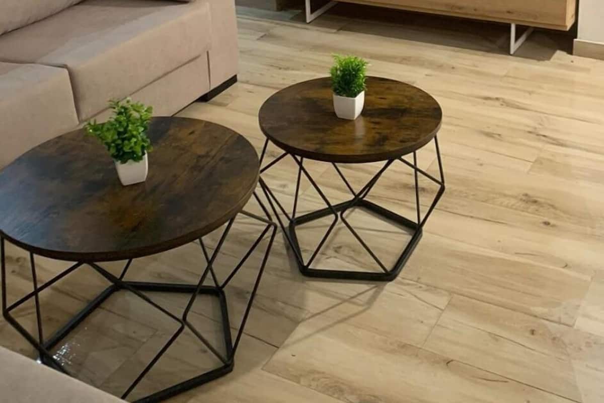 Ein Wohnzimmer mit einem beige farbenen Sofa, zwei runden Couchtischen mit Pflanzen, einer Holz-TV-Konsole und einem großen Flachbildfernseher.