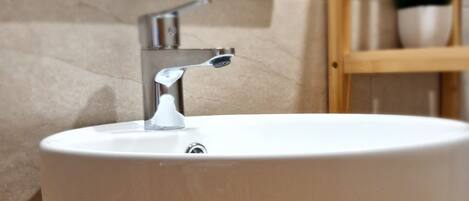 Un baño con un lavamanos redondo blanco, un tocador de madera, un espejo y una planta en maceta.