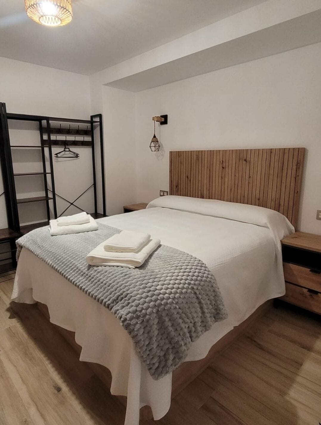 Un dormitorio con cama, cabecera de madera, perchero y mesita de noche.