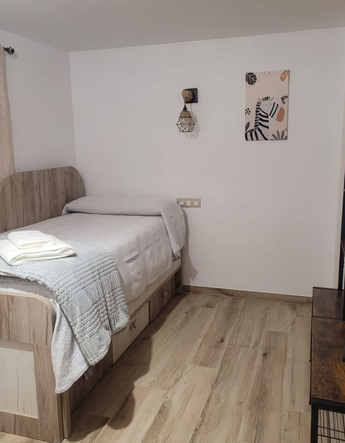 Un dormitorio pequeño y ordenado con cama, una lámpara en la pared y una pequeña decoración mural.