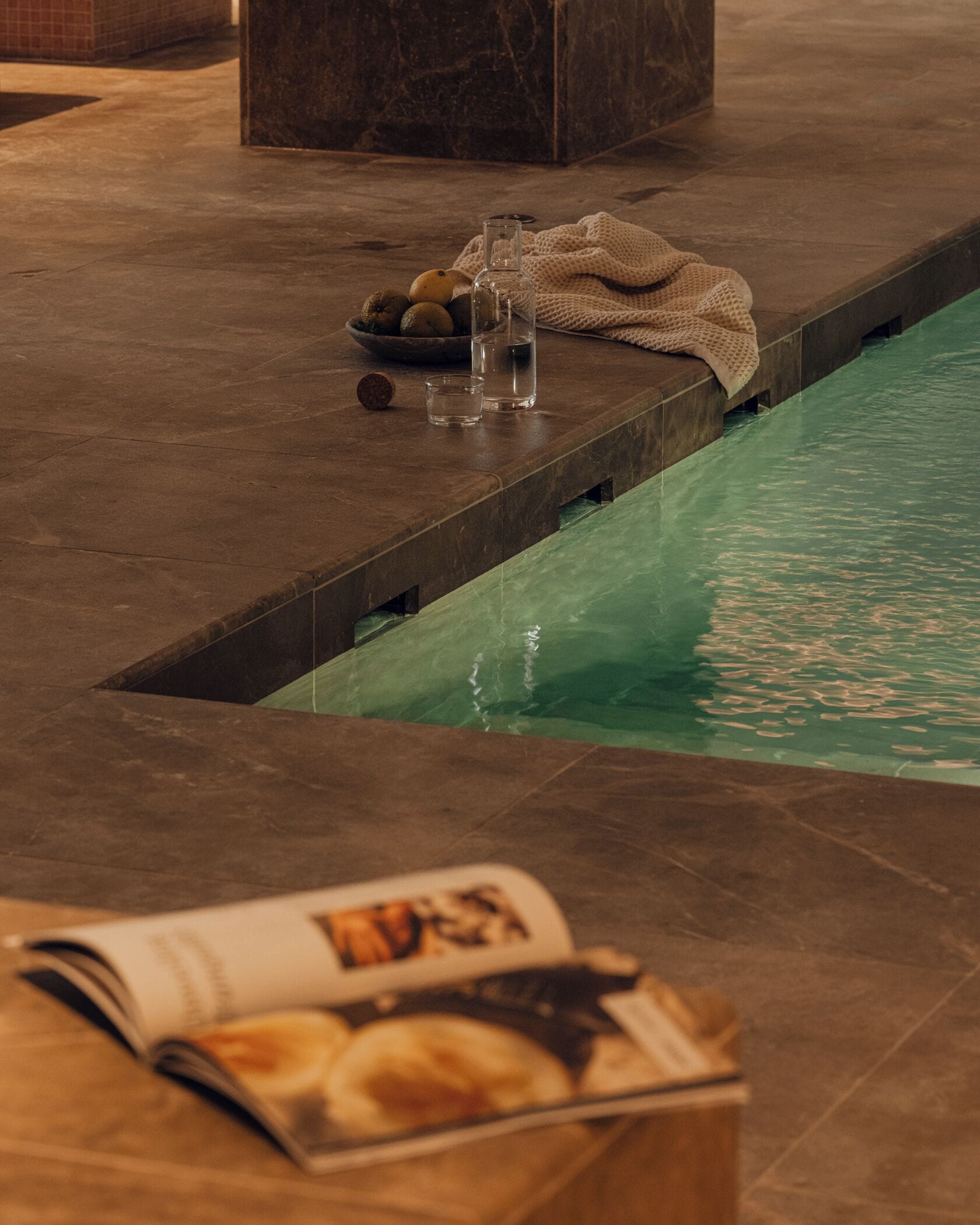 Un espace spa avec une piscine, un magazine posé sur une table et une serviette sur le bord de la piscine.