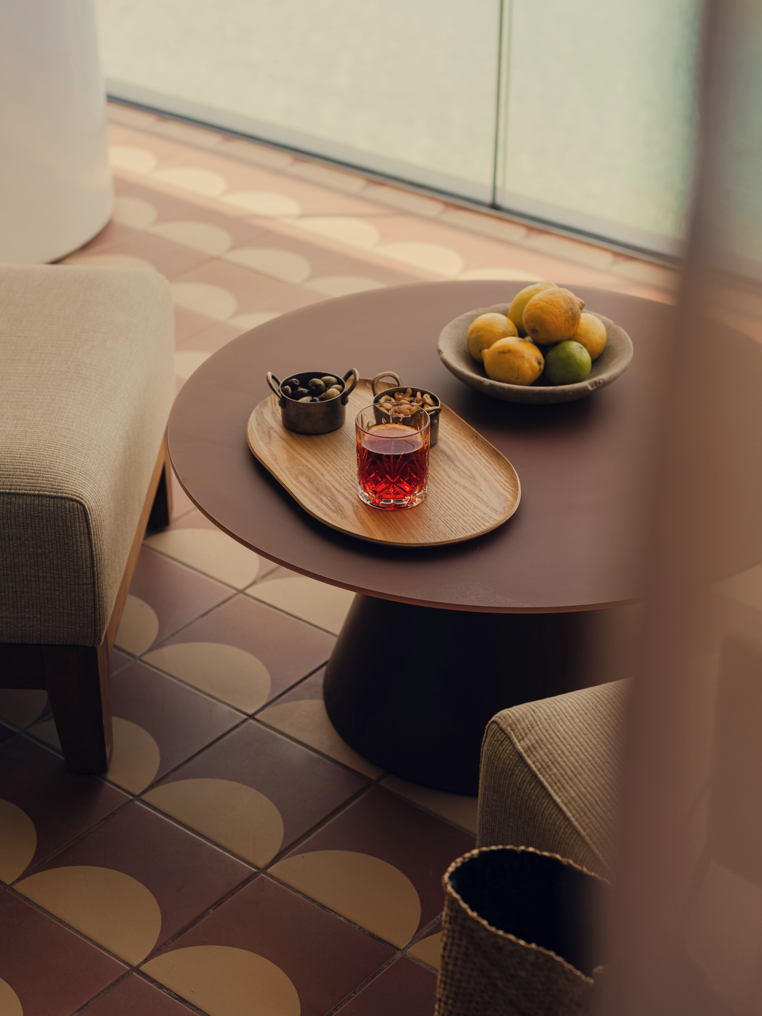 Une table ronde sur laquelle se trouve un plateau avec un verre contenant un liquide rouge, un bol de citrons et un petit pot de noix.