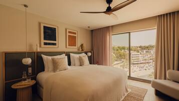 A bedroom with a large bed, a ceiling fan, a view of a beach, and a cityscape.
