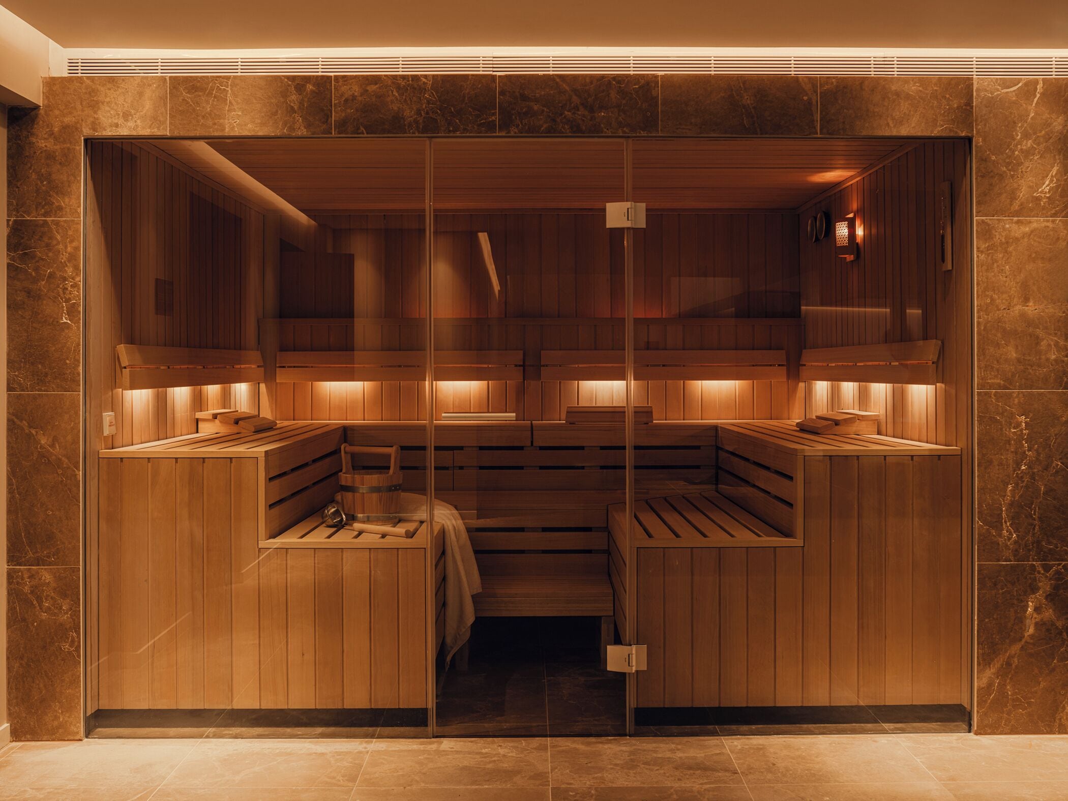 A sauna with wooden benches and a central bench, separated by glass walls.