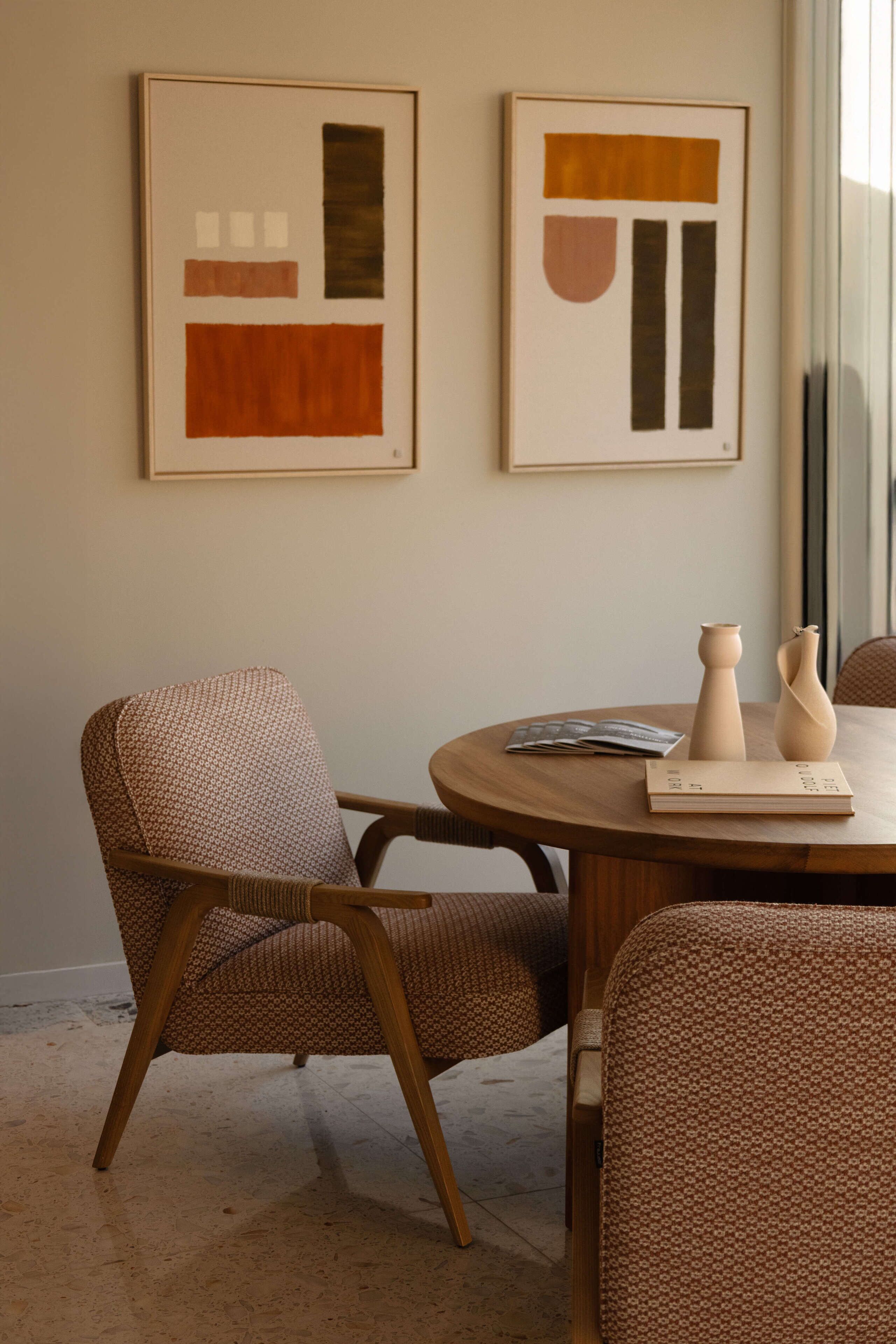 A dining area with a round wooden table, two chairs, and abstract artwork on the wall.