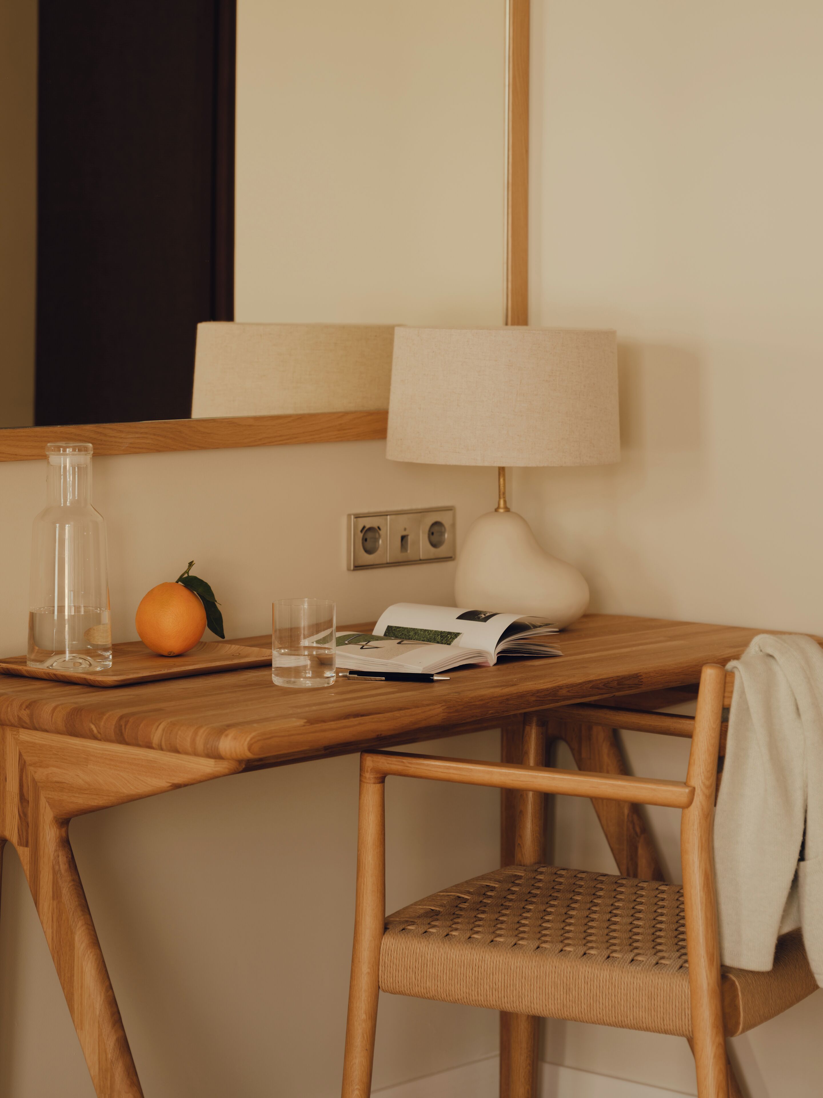 A wooden desk with a lamp, a bottle, glasses, and a book.