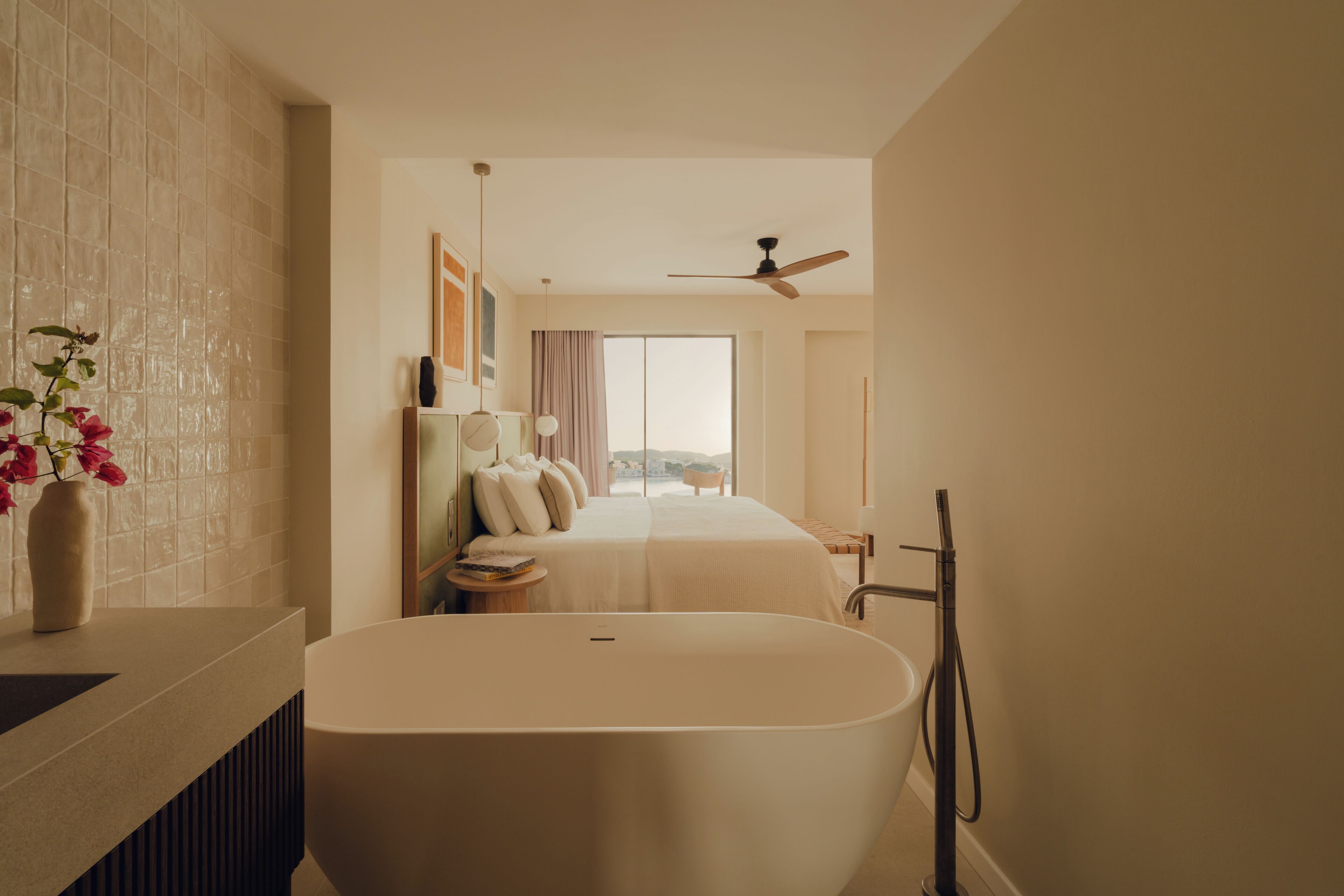 A modern bathroom with a freestanding bathtub, a vanity with a vase of flowers, and a large bed with a view of the city.