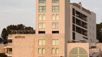 Un immeuble à plusieurs étages, reconnaissable à son grand panneau « aethos », qui présente un mélange de fenêtres rectangulaires et en arc de cercle, ainsi qu’une façade en pierre.