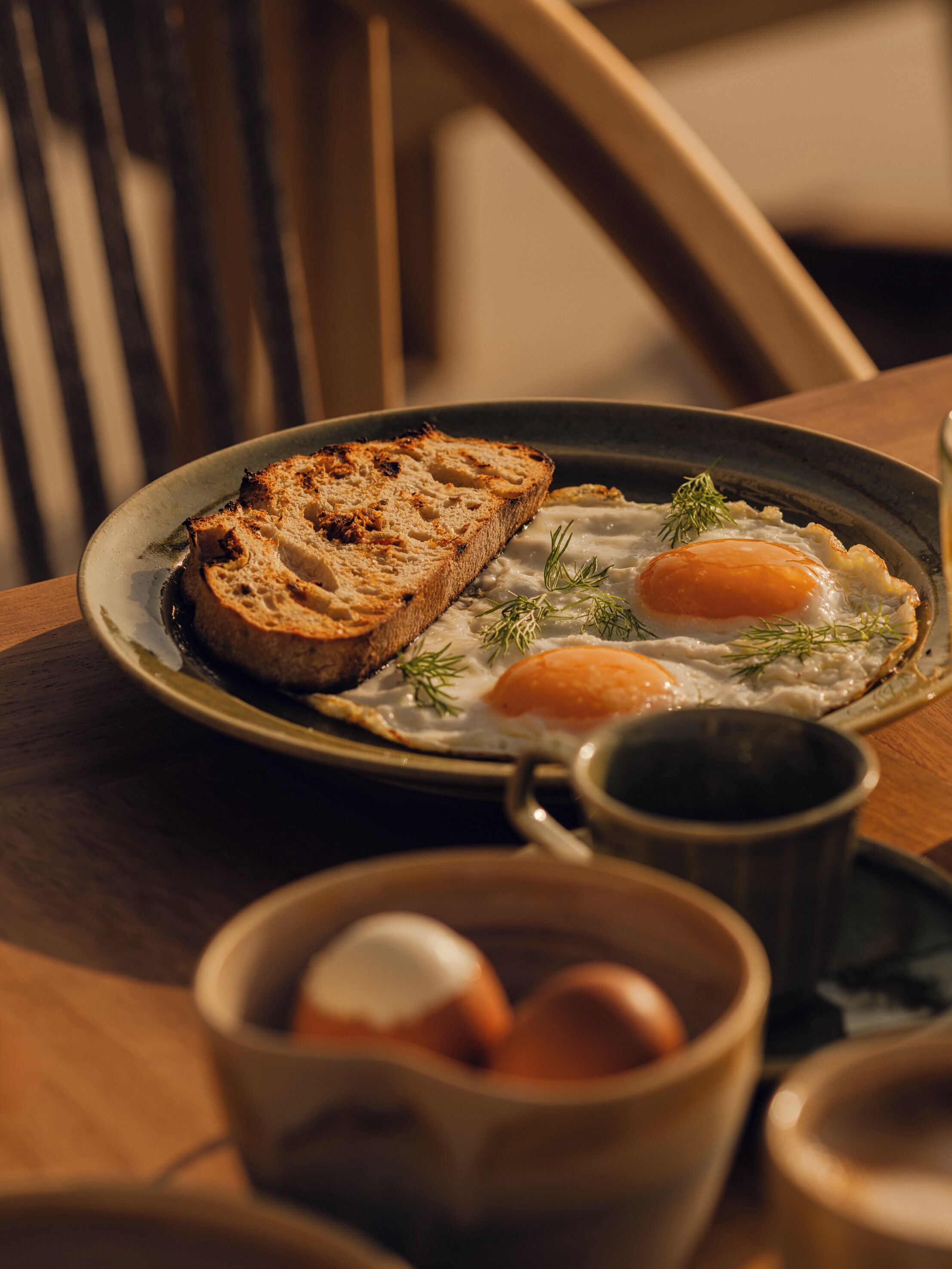 A plate with toast and eggs, a mug, and a bowl of eggs on a wooden table.