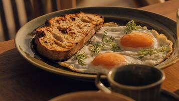 A plate with toast and eggs, a mug, and a bowl of eggs on a wooden table.