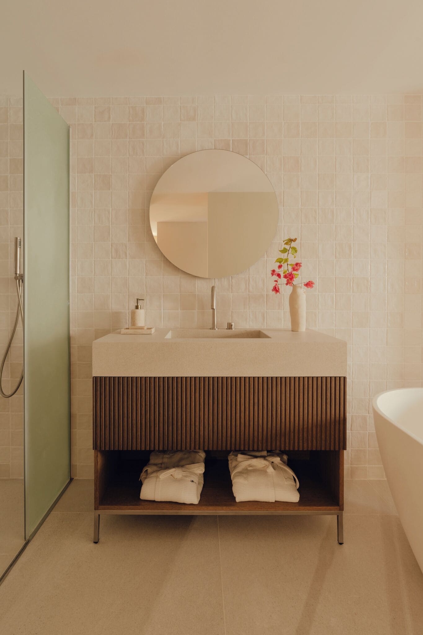 A modern bathroom with a round mirror, a sink, and a shower.
