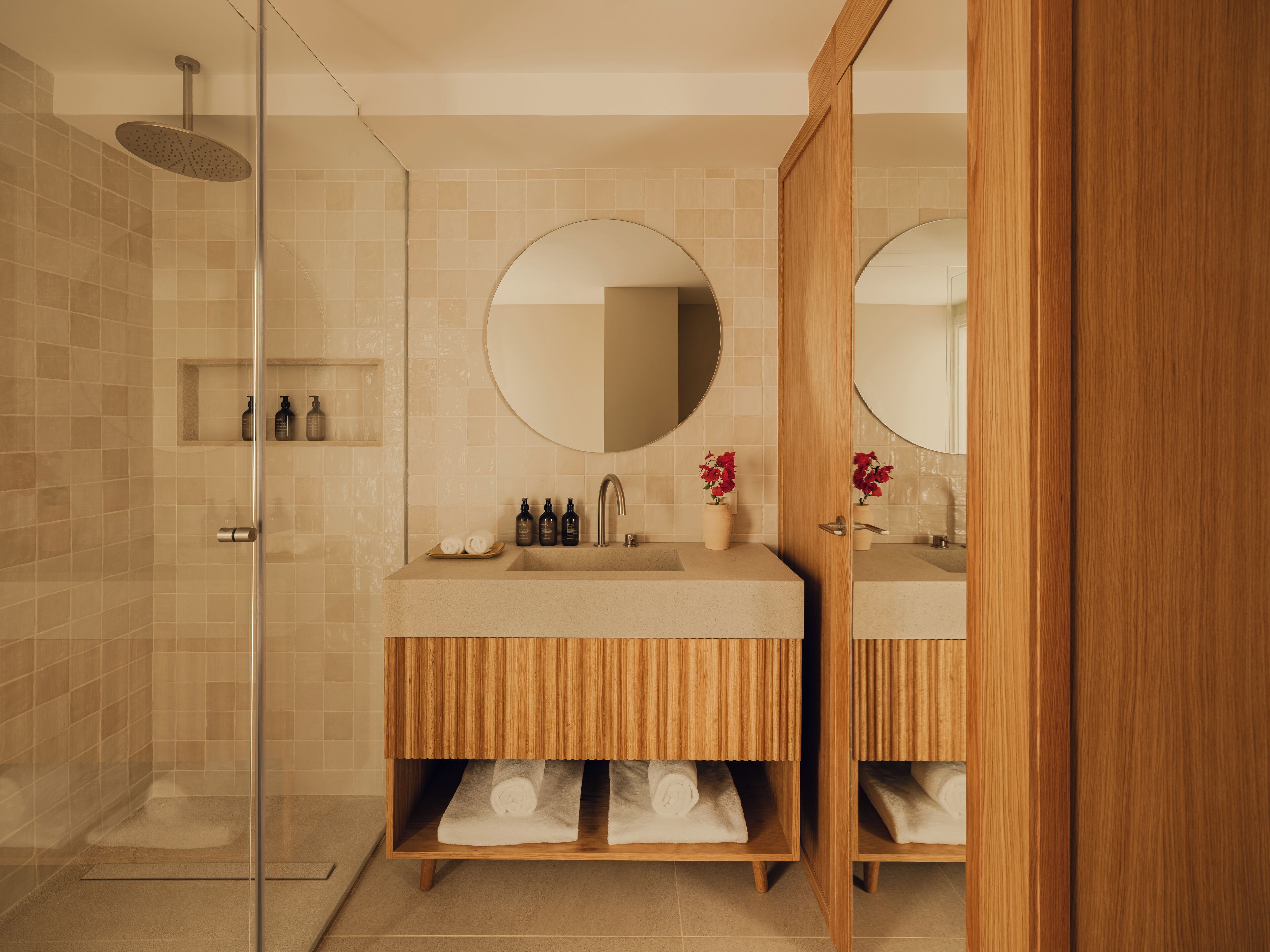 A modern bathroom with a glass shower enclosure, wooden vanity with a mirror, and a sink.