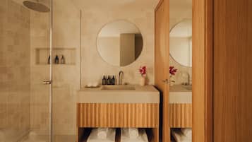 A modern bathroom with a glass shower enclosure, wooden vanity with a mirror, and a sink.