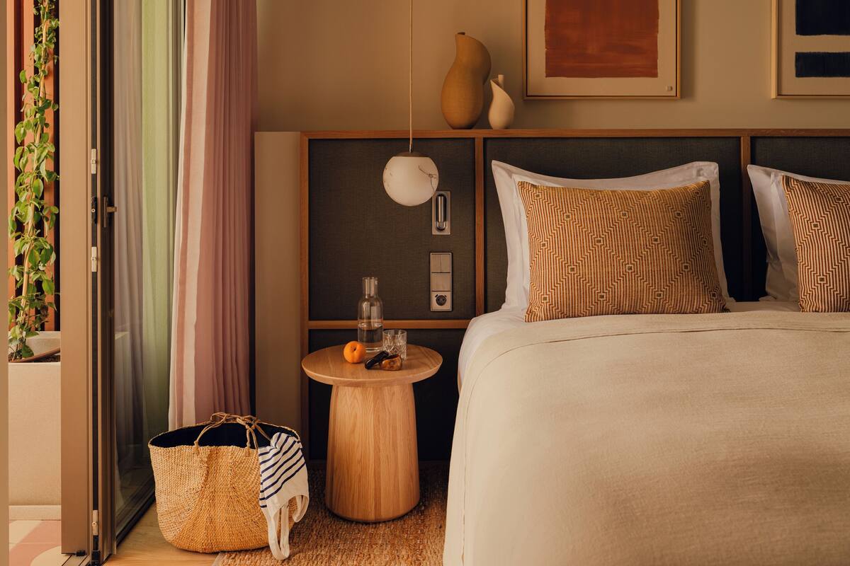 A hotel room with a bed, bedside table, lamp, and a view of the outdoors.