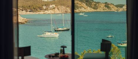 Una habitación con vista al mar, que incluye una mesa y sillas orientadas hacia la ventana.