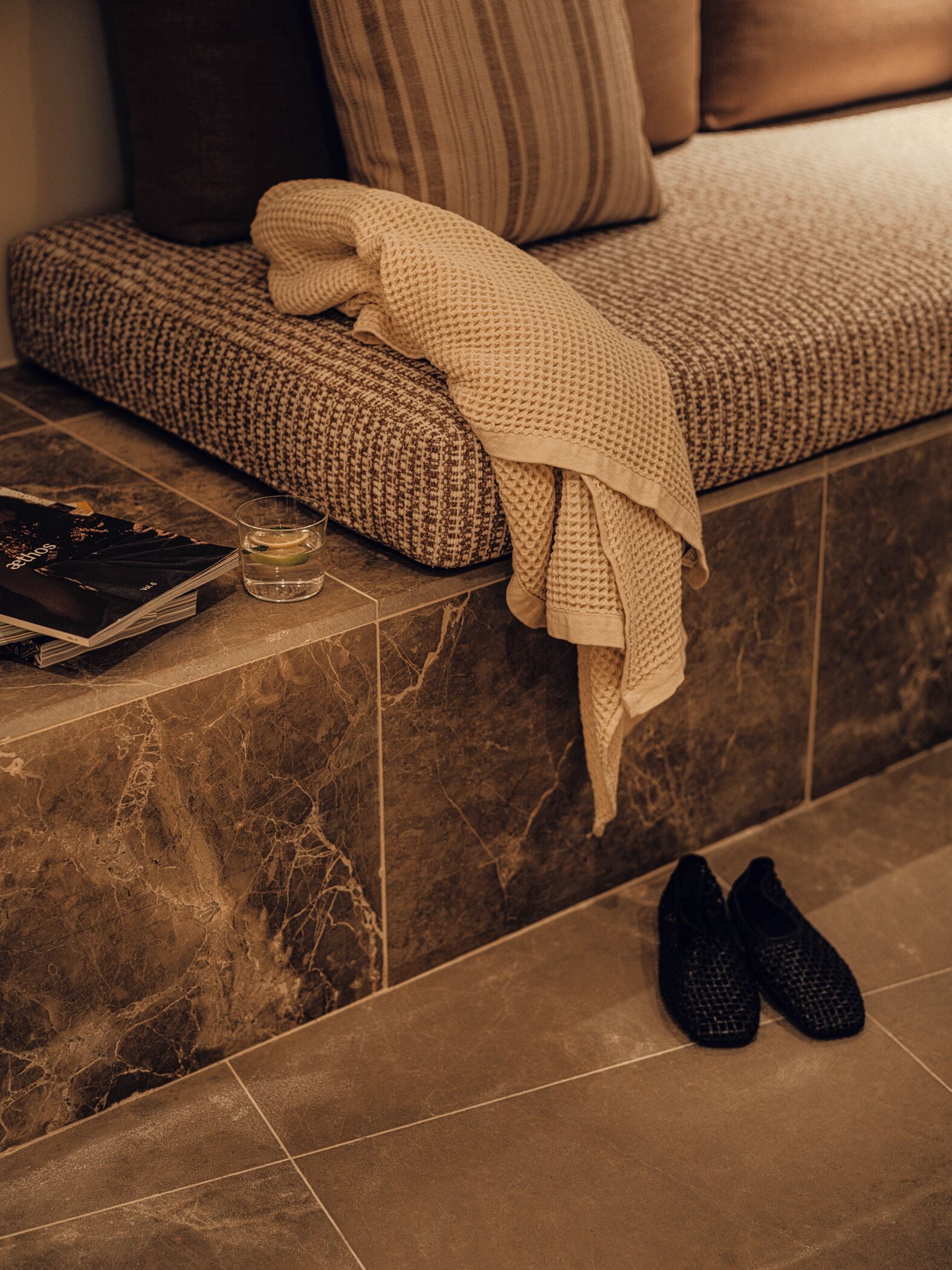 A cozy seating area with a patterned cushion, a folded blanket, and a pair of shoes on the floor.