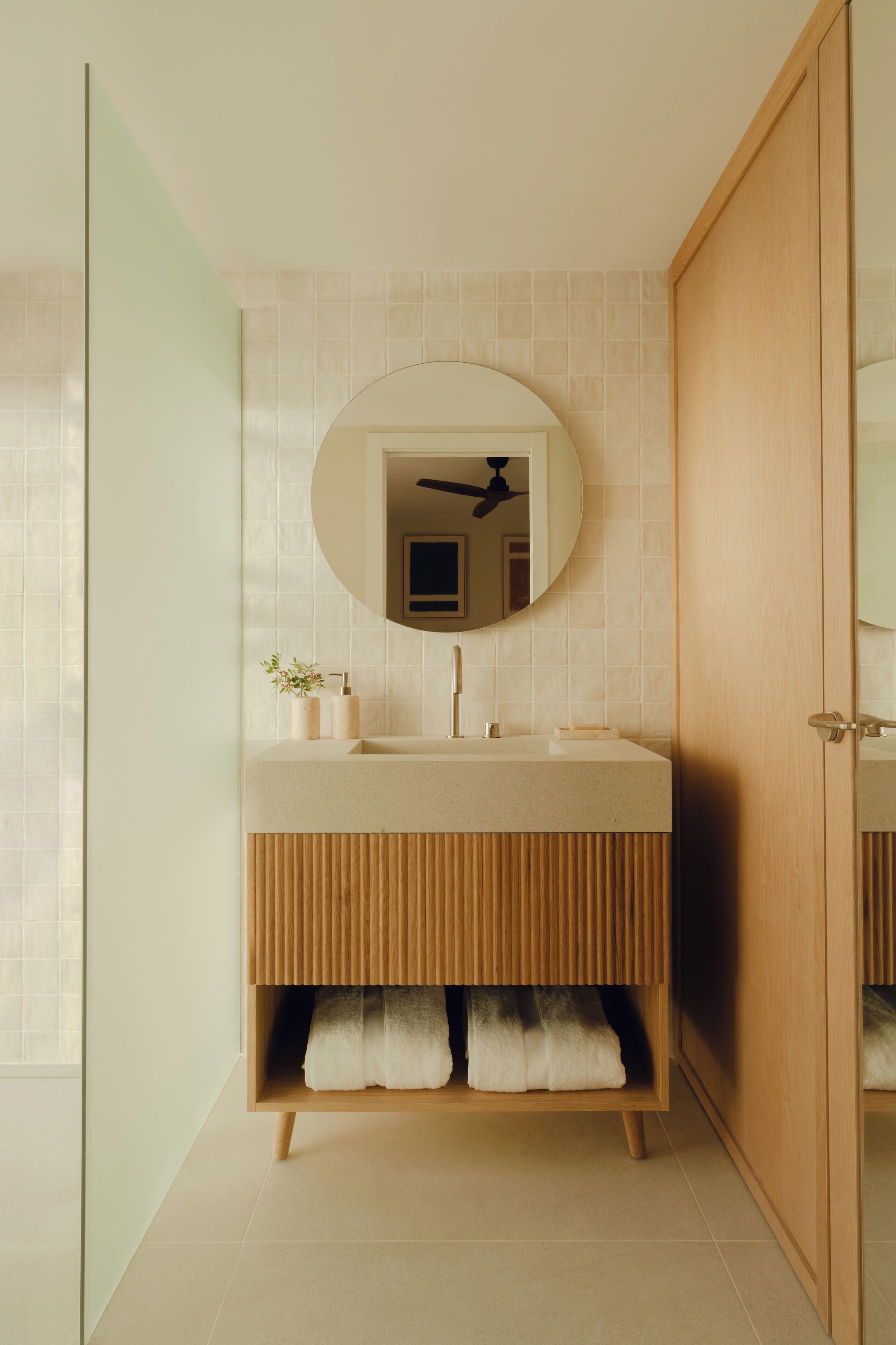 A modern bathroom with a wooden vanity, a round mirror, and a built-in towel rack.