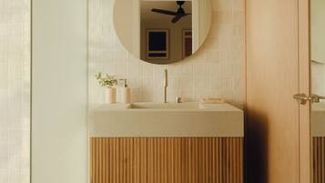 A modern bathroom with a wooden vanity, a round mirror, and a built-in towel rack.