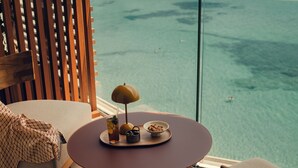 A balcony with a table set for two, overlooking a beach and ocean.