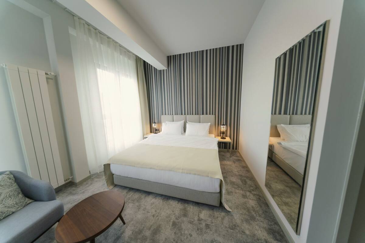 Ein modernes Hotelzimmer mit einem großen Bett, Nachttischen mit Lampen, einer Couch und einem kleinen Tisch.