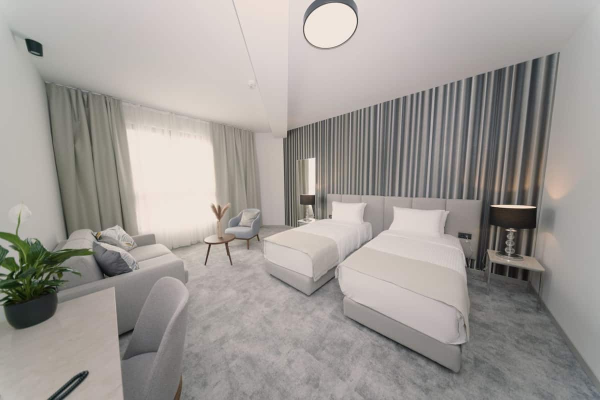 Ein modernes Hotelzimmer mit einem großen Bett, einem Einzelbett, einer Couch, einem Schreibtisch und einer Zimmerpflanze.