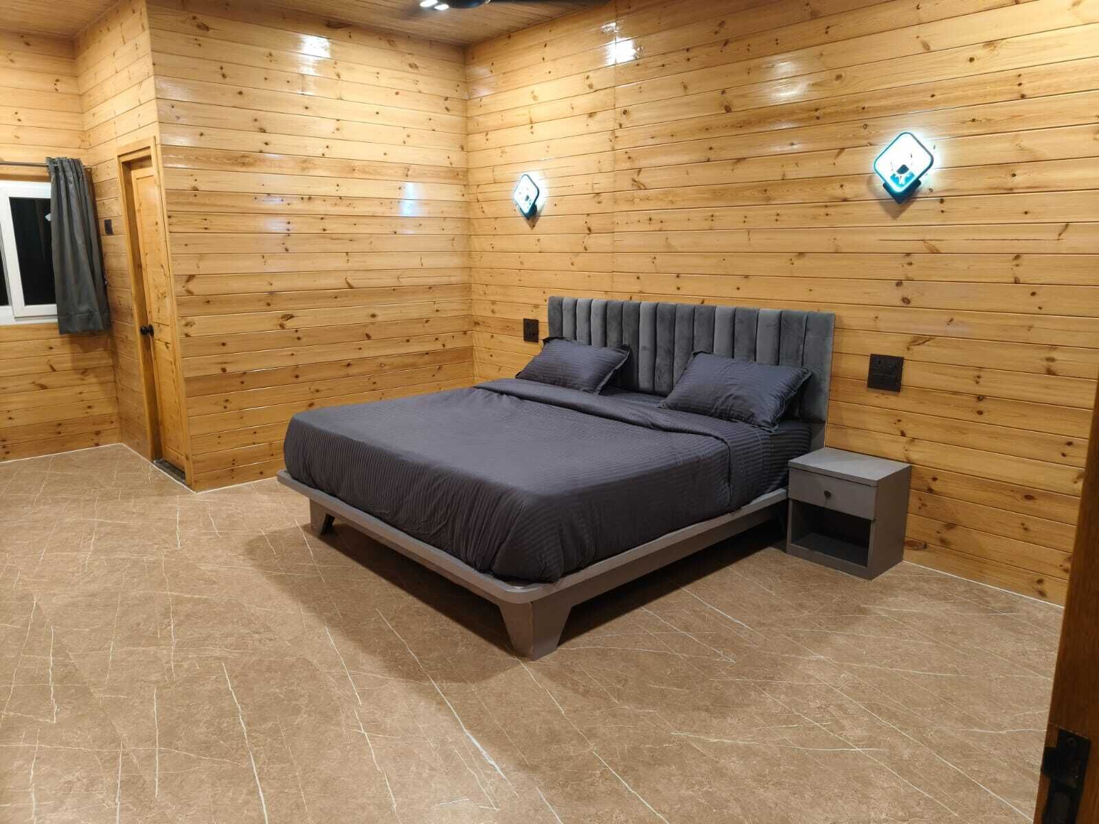 A wooden-paneled room with a bed, bedside tables, and wall-mounted light fixtures.