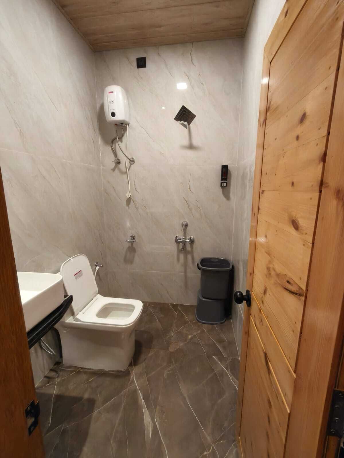 Ein kleines Badezimmer mit Toilette, Waschbecken, Dusche und Holztür.