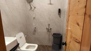 Ein kleines Badezimmer mit Toilette, Waschbecken, Dusche und Holztür.
