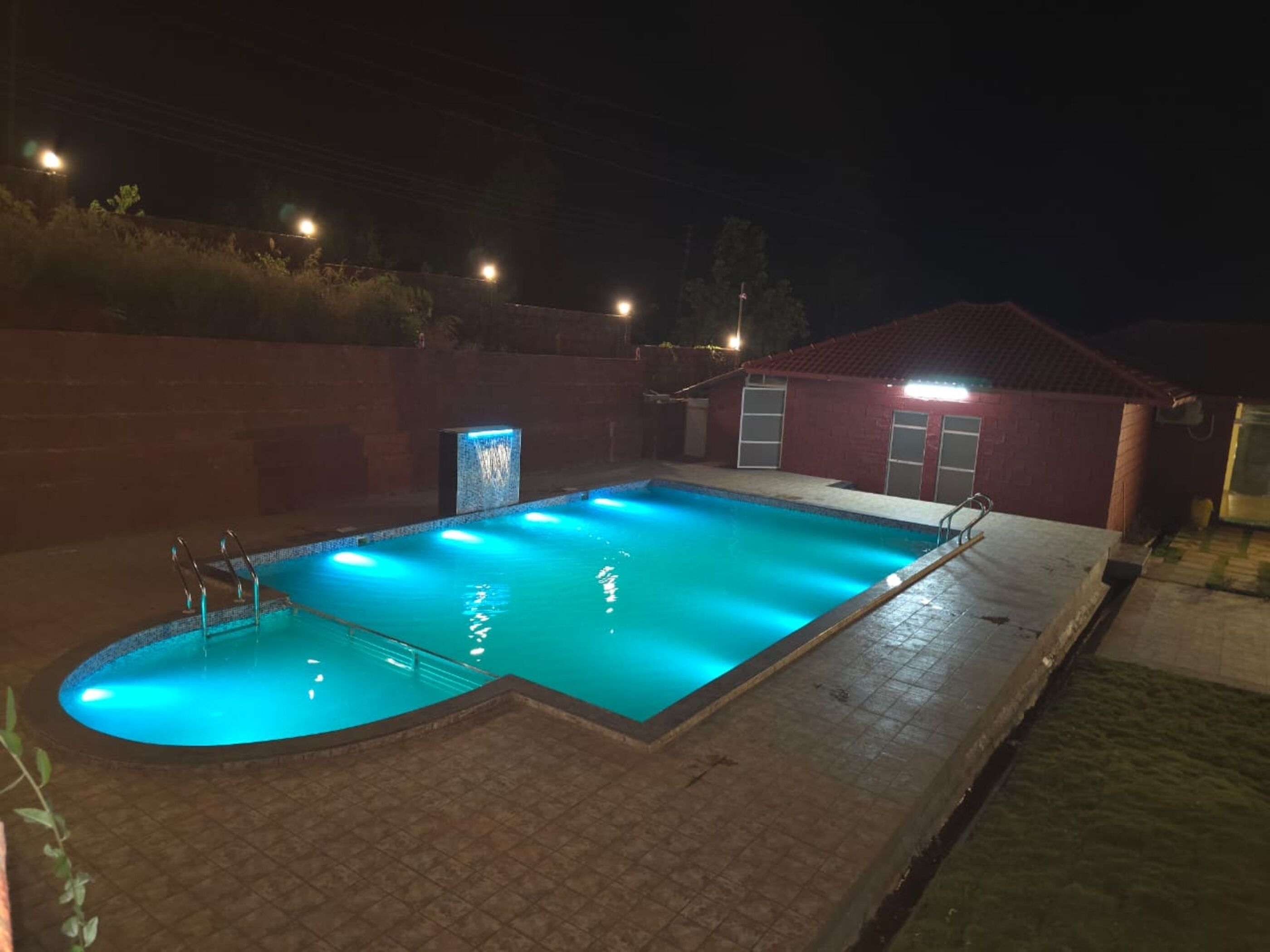 A rectangular swimming pool with a tiled deck and a small waterfall feature.