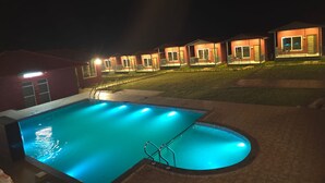Μια πισίνα με καθαρό νερό και διακοσμητικό στοιχείο, που περιβάλλεται από μια πλακόστρωτη περιοχή και βρίσκεται δίπλα σε μια σειρά από κτίρια από τούβλα, με εμφανείς πόρτες και παράθυρα.