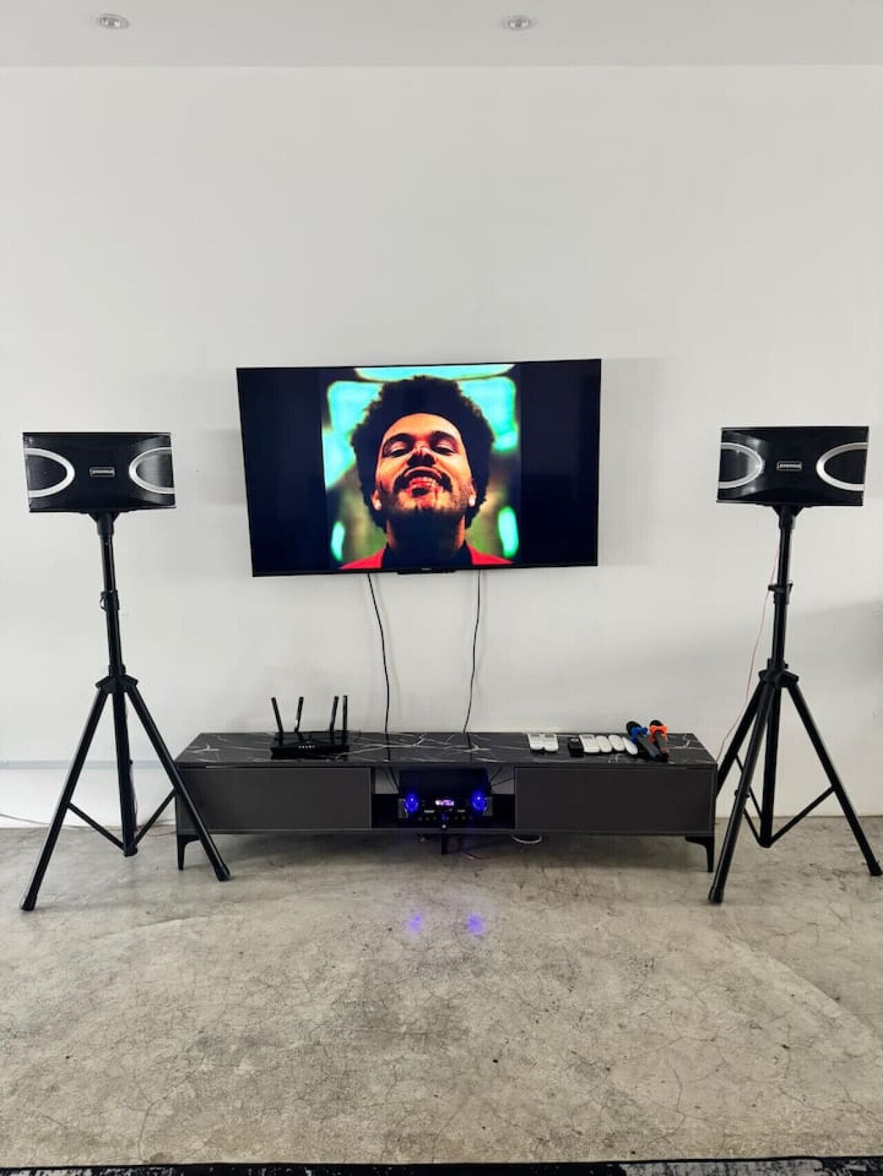A room with a large flat-screen TV mounted on the wall, flanked by two black speakers on stands.