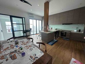 Une cuisine moderne dotée d’un îlot central, d’un coin repas avec une table et d’une grande fenêtre qui laisse entrer la lumière naturelle.