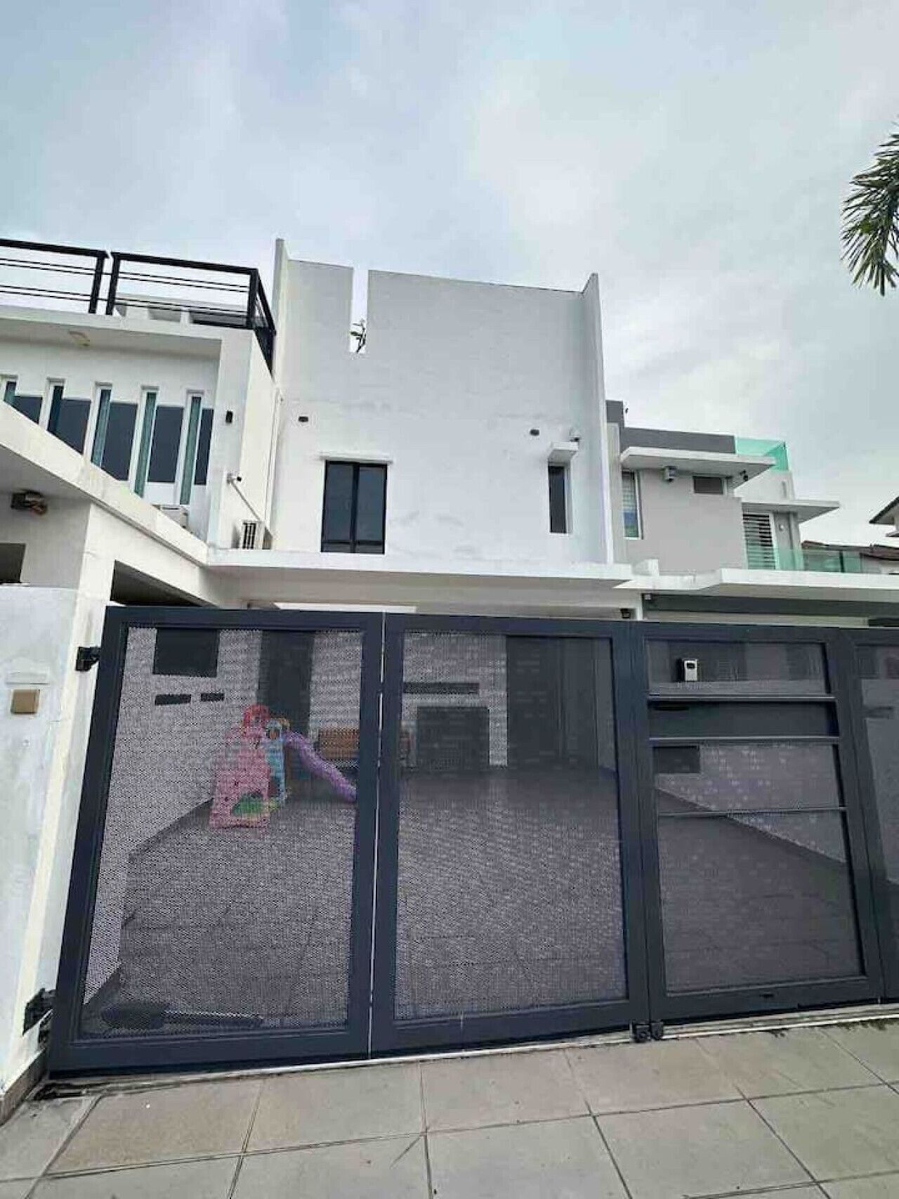 Une maison moderne à deux étages, dotée d’un grand portail de garage et d’un balcon.