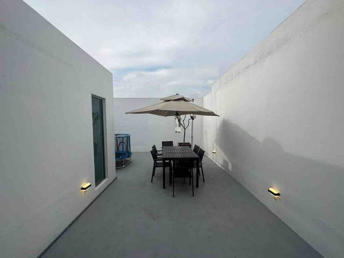 A patio with a table and chairs, an umbrella, and wall-mounted lights.
