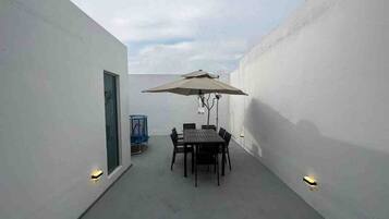 A patio with a table and chairs, an umbrella, and wall-mounted lights.