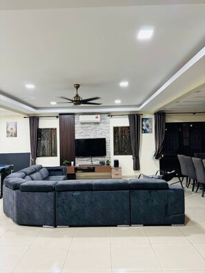 A modern living room with a sectional sofa, a flat-screen TV, a ceiling fan, and a dining area with chairs.