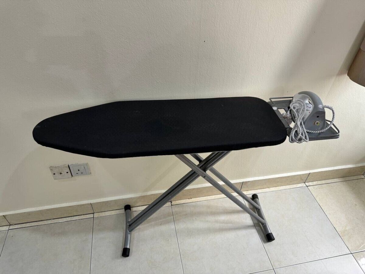 A portable ironing board with a black surface and a metallic frame, placed on a tiled floor against a plain wall.