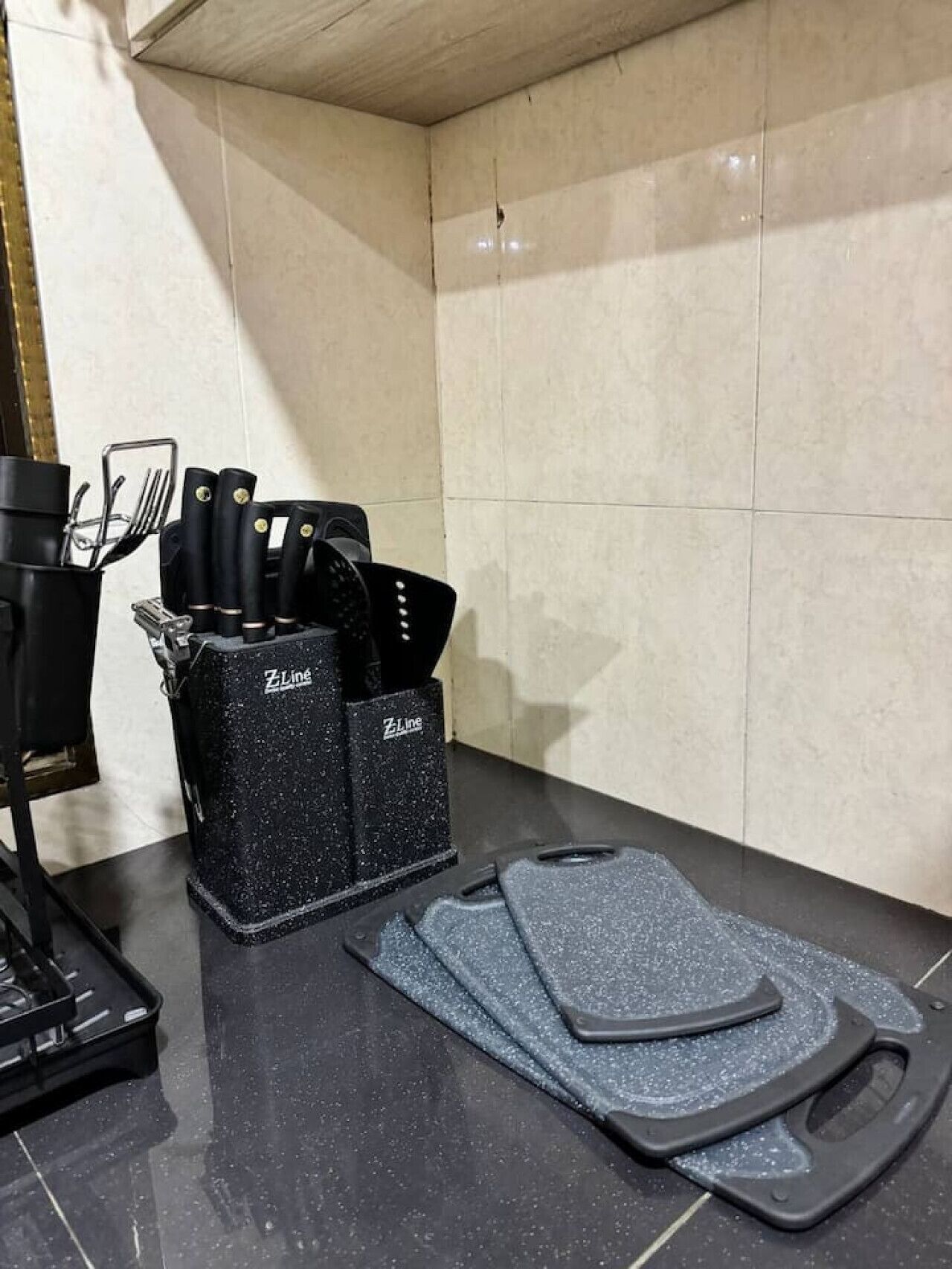 A kitchen area with a black Z-Line spice rack holding knives and a spatula, a black stove, and a pair of gray cutting mats on the counter.