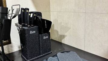 A kitchen area with a black Z-Line spice rack holding knives and a spatula, a black stove, and a pair of gray cutting mats on the counter.