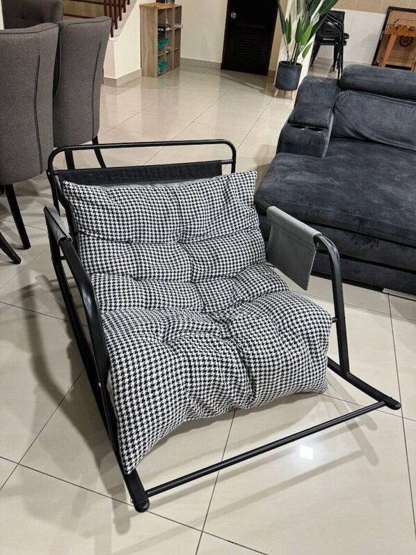 A black metal chair with a houndstooth cushion in a modern living room with a grey sofa and a wooden cabinet.