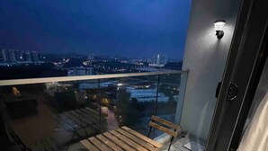 Ein Balkon mit Glastisch und Stühlen, Blick auf die Stadt im Abendlicht, und eine moderne Gebäudefassade.