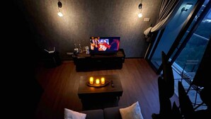 Ein modernes Wohnzimmer mit Fernseher, einem kleinen Tisch mit Kerzen und einer Couch mit Kissen.