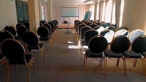 A conference room with rows of chairs facing a projection screen, a podium, and a window with curtains.