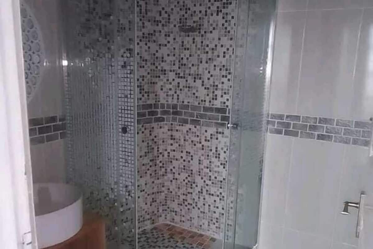 A shower with a glass door, tiled walls, and a small step leading to the shower area.